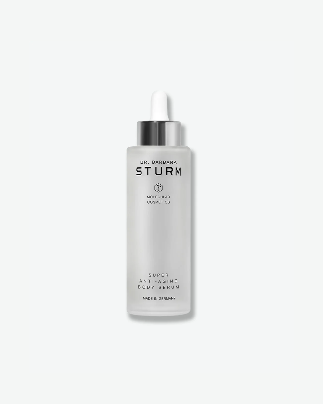 A product shot of a tall Dr. Barbara Sturm Super Anti-Aging Body Serum bottle, centered on a light gray background. The large cylindrical bottle is made of frosted glass, filled with a cloudy liquid, and topped with a metallic silver dropper cap and a white rubber bulb.