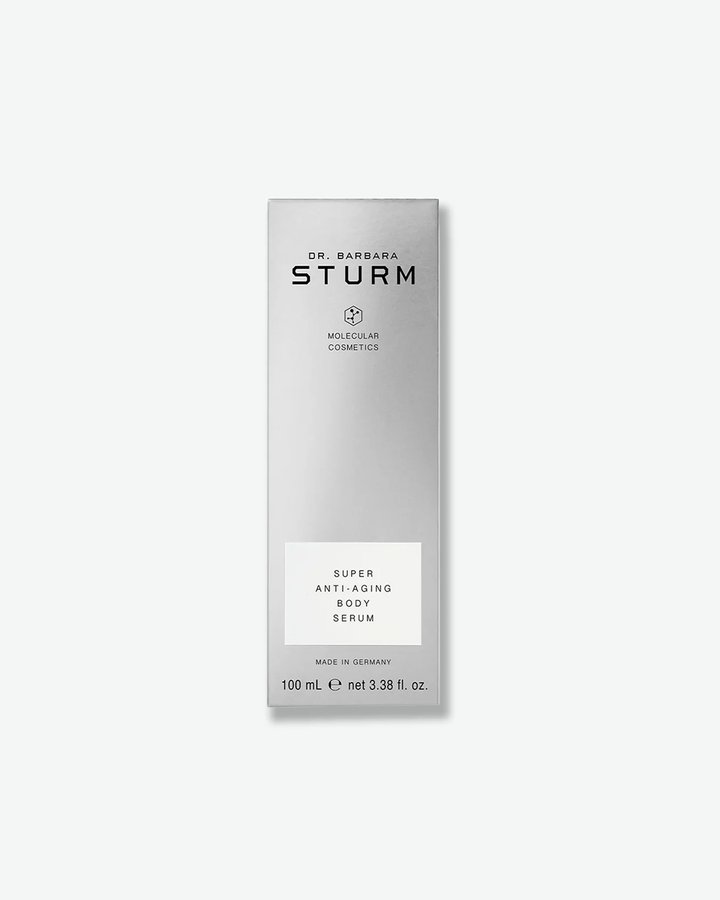 A product shot of the tall, slender silver box for Dr. Barbara Sturm Super Anti-Aging Body Serum. It features minimalist black text with a clean white box highlighting the product name. The bottom shows "100 mL e net 3.38 fl. oz."