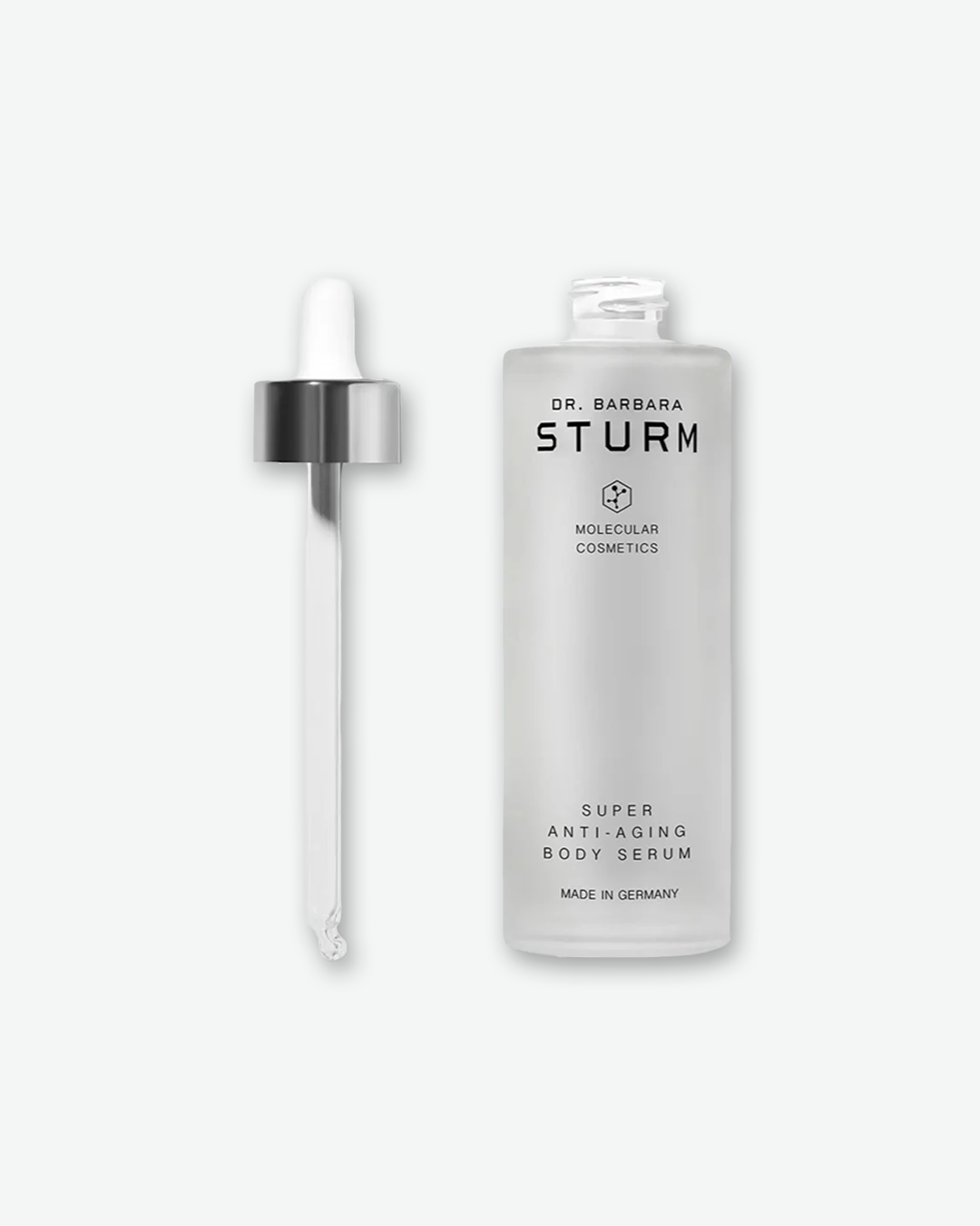 A product shot of the Dr. Barbara Sturm Super Anti-Aging Body Serum unscrewed on a light gray background. The frosted body serum bottle stands on the right, while the long glass pipette wand with its shiny silver cap stands upright to its left.