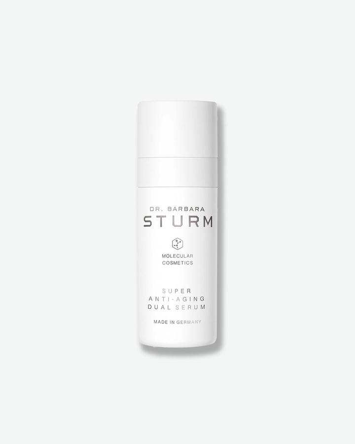 A product shot of a Dr. Barbara Sturm Super Anti-Aging Dual Serum bottle, centered against a light gray background. The tall, cylindrical white bottle features a matching opaque pump cap. The minimalist black text on the front reads "DR. BARBARA STURM", the molecular hexagon logo, "MOLECULAR COSMETICS", "SUPER ANTI-AGING DUAL SERUM", and "MADE IN GERMANY".