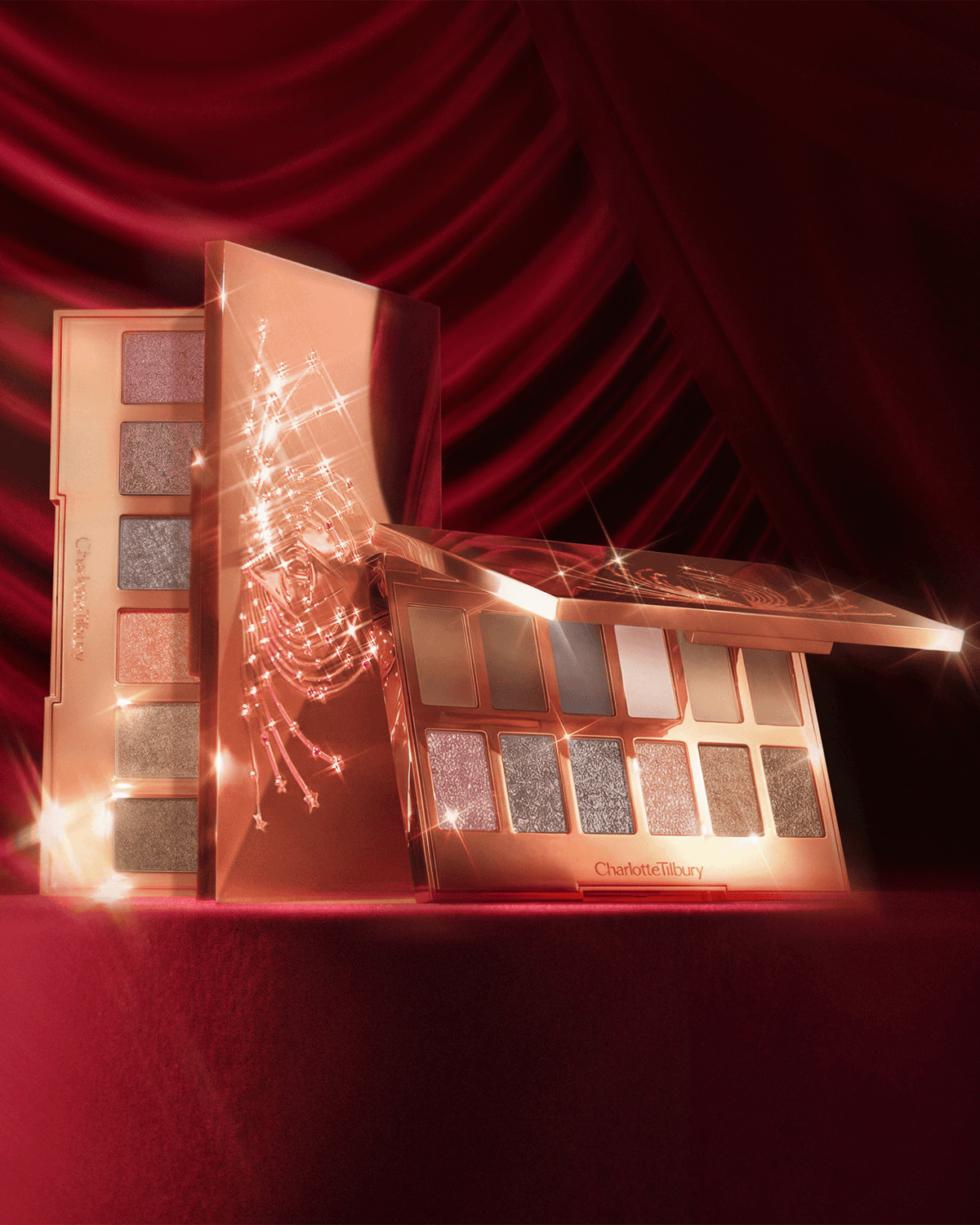 Charlotte Tilbury Hollywood Flawless Light Tricks Eye Palettes displayed on rich red velvet with sparkling rose gold packaging.