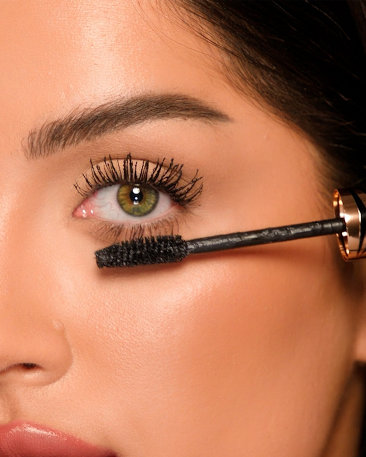 Close-up of a model’s eye with Charlotte Tilbury Exagger-Eyes Volume Mascara wand positioned beneath the lashes.