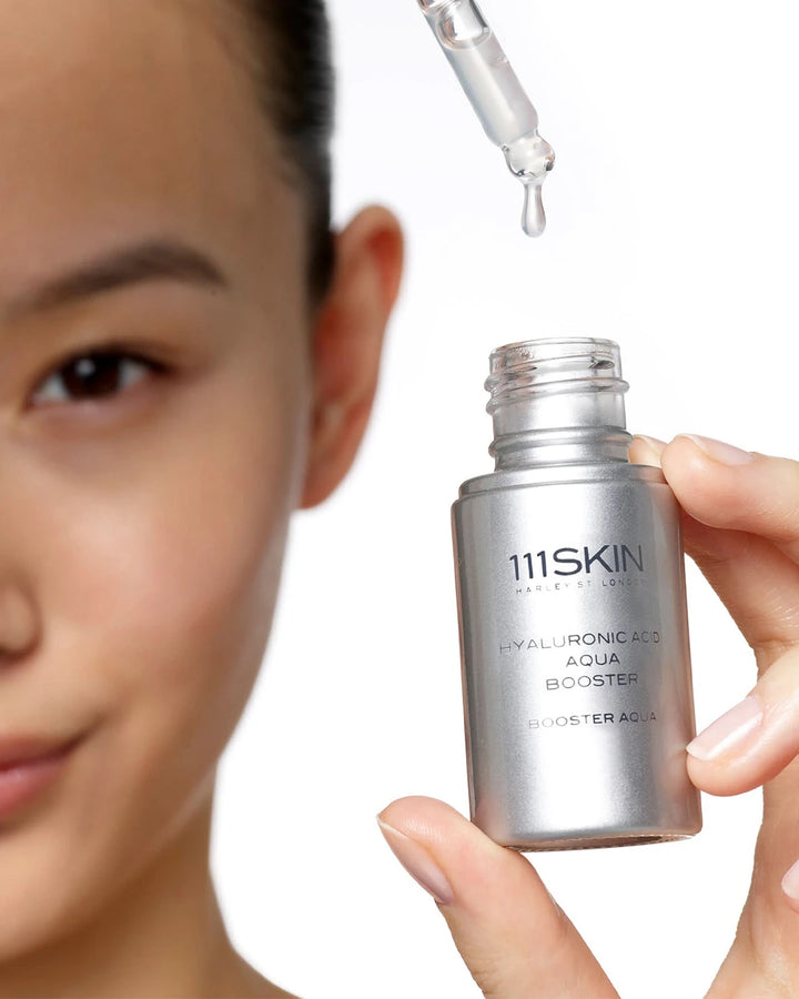 111SKIN skincare product with dropper held by a hand, close-up of face.