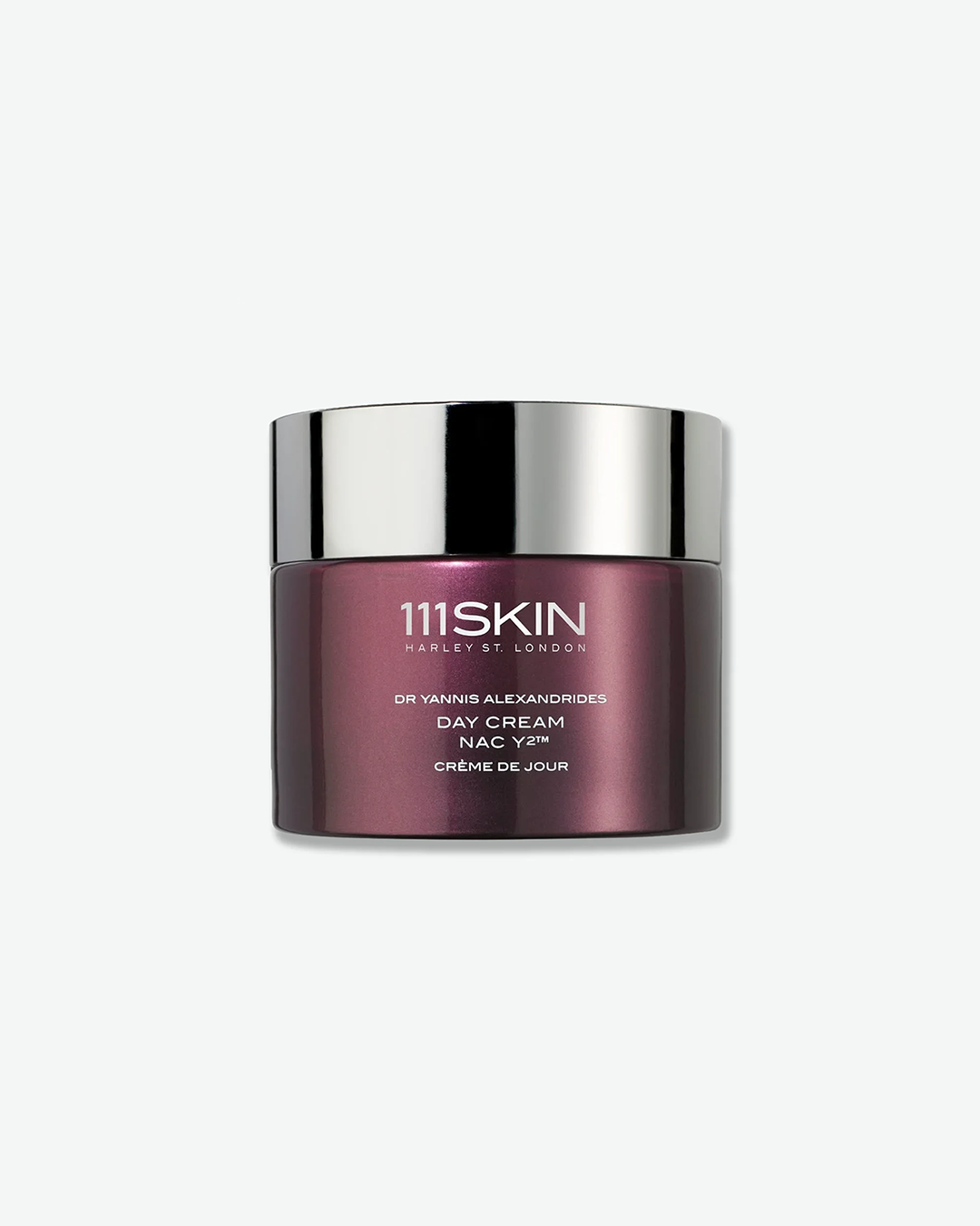 A product shot of a 111SKIN Day Cream NAC Y2 jar, centered against a plain light gray background. The cylindrical jar is made of a glossy, deep metallic purple glass and is sealed with a reflective chrome silver screw-on lid. The front displays white text detailing the brand name, product, formulation, and the French translation "CRÈME DE JOUR".