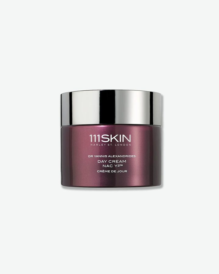 A product shot of a 111SKIN Day Cream NAC Y2 jar, centered against a plain light gray background. The cylindrical jar is made of a glossy, deep metallic purple glass and is sealed with a reflective chrome silver screw-on lid. The front displays white text detailing the brand name, product, formulation, and the French translation "CRÈME DE JOUR".