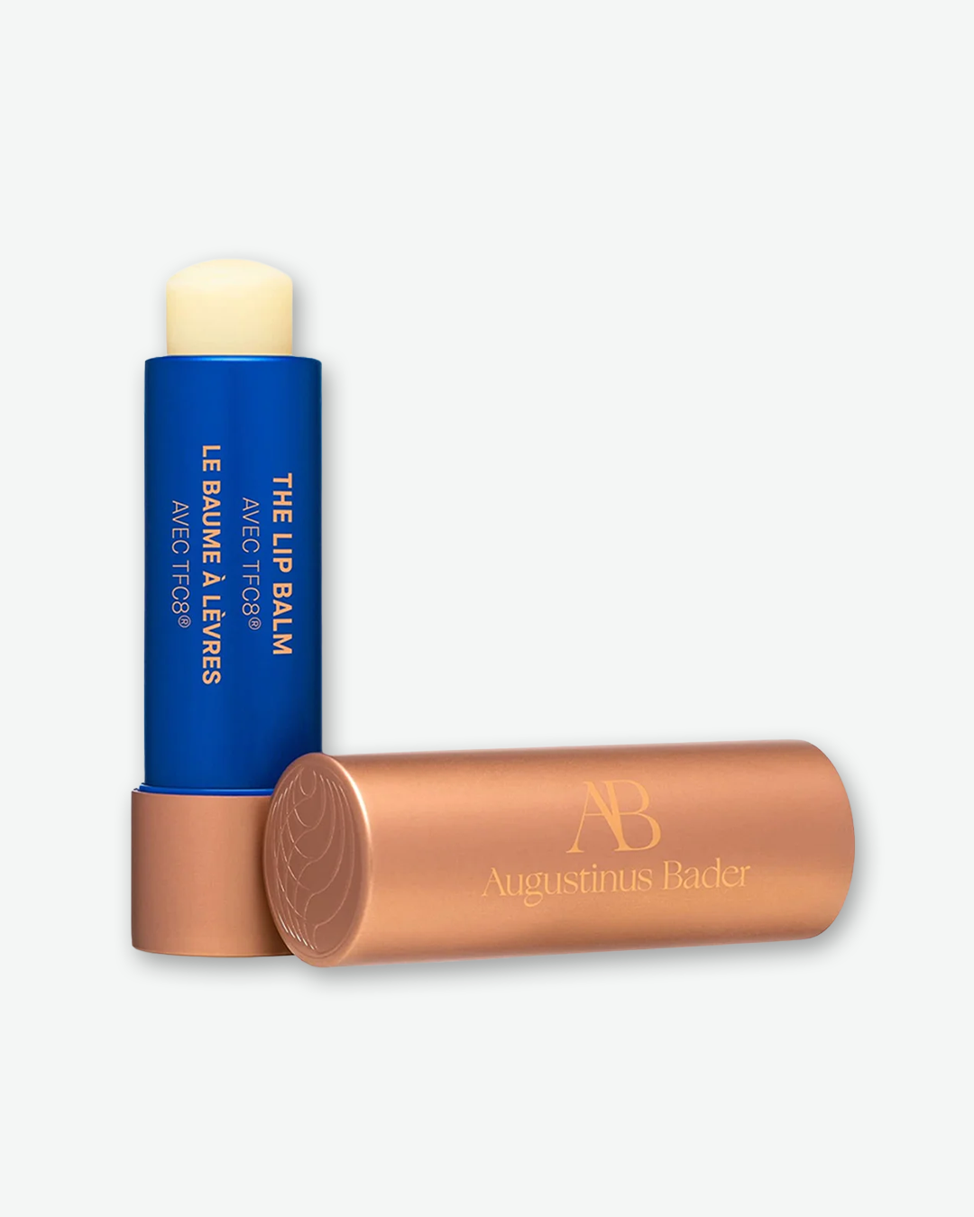 An open Augustinus Bader The Lip Balm with Advanced TFC8 showing the cream-colored balm formula in a bright blue tube next to its metallic copper cap.
