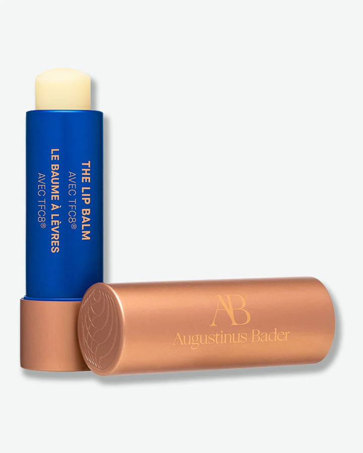 Blue Augustinus Bader lip balm stick with bronze cover off on a white background