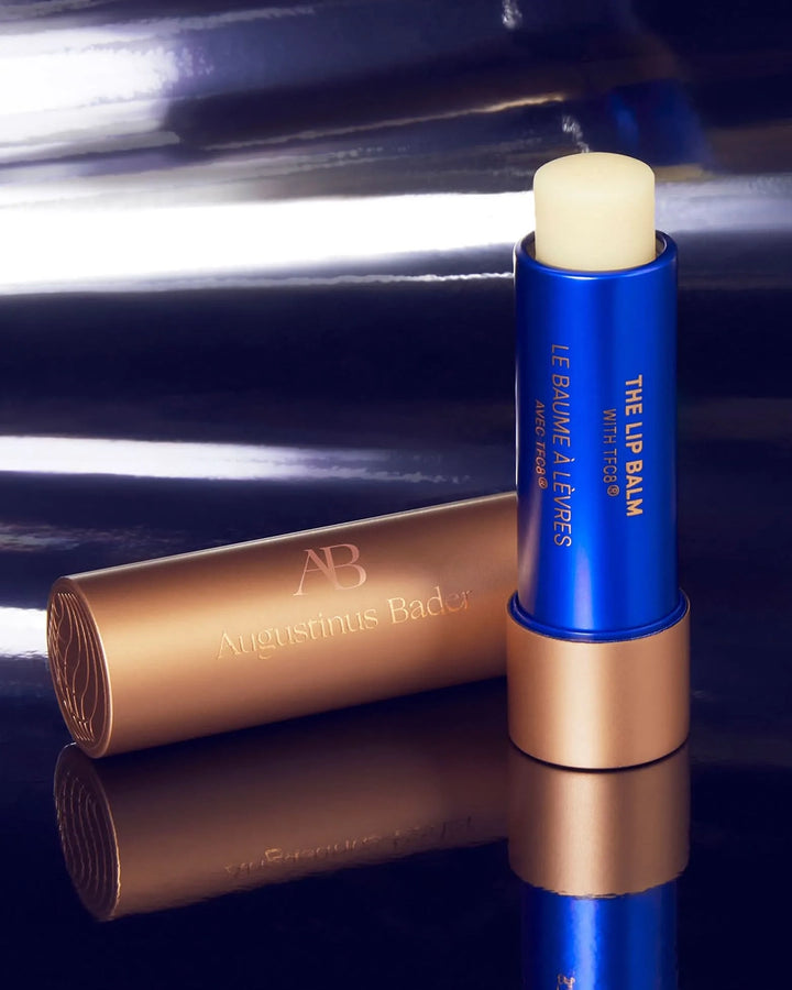 Blue lip balm with beige applicator and gold tube on a reflective surface