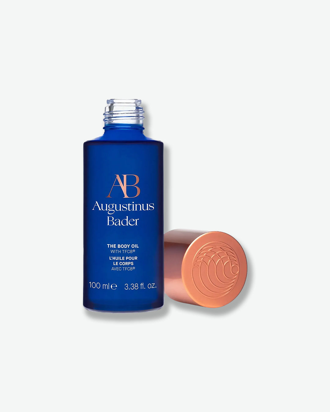 Blue bottle of Augustinus Bader body oil with a pink cap on a white background