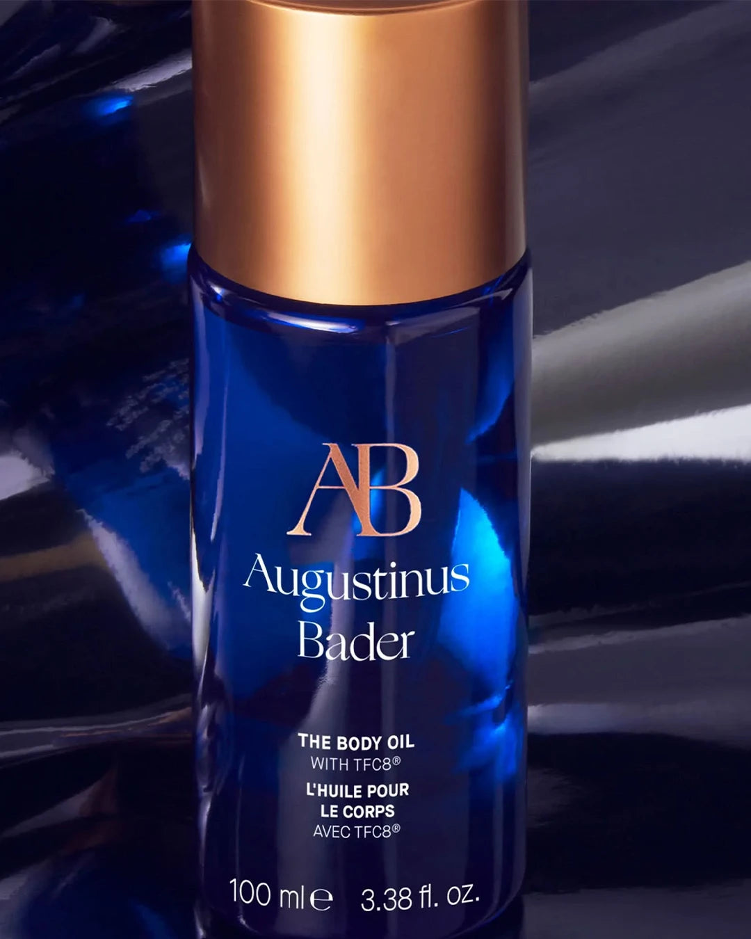 Blue bottle of Augustinus Bader body oil with gold cap on a reflective surface