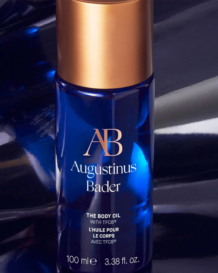 Blue bottle of Augustinus Bader body oil with gold cap on a reflective surface