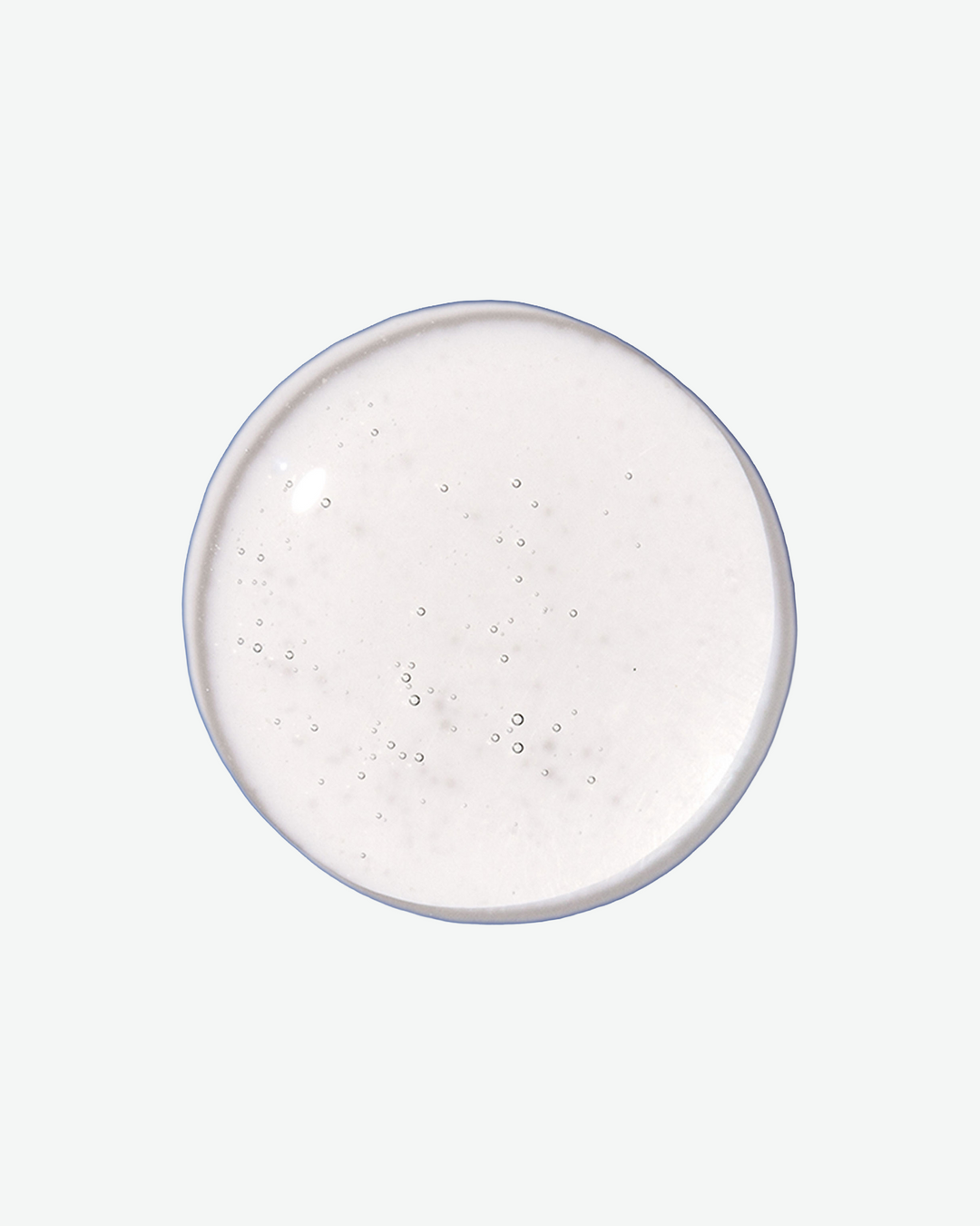 A top-down close-up view of a perfectly round, clear liquid droplet containing tiny air bubbles against a light gray background.