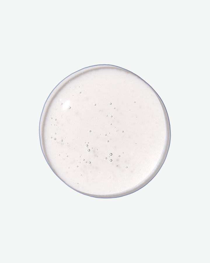 A top-down close-up view of a perfectly round, clear liquid droplet containing tiny air bubbles against a light gray background.