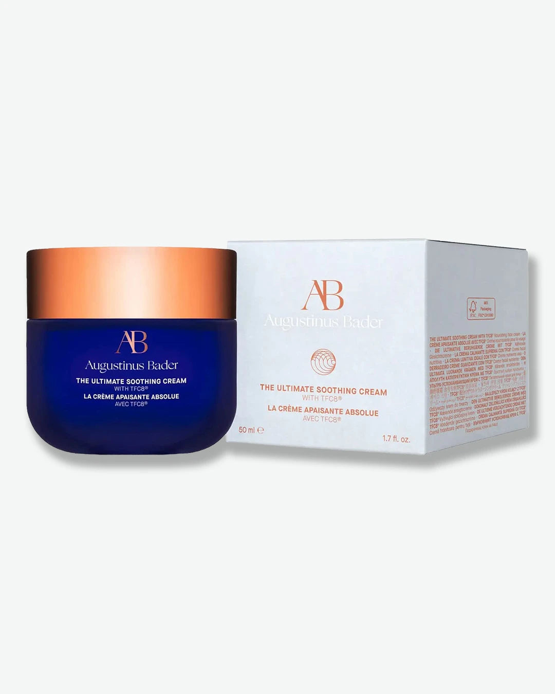 Augustinus Bader The Ultimate Soothing Cream jar with blue body and bronze lid stood next to its light grey packaging box with bronze text on a white background