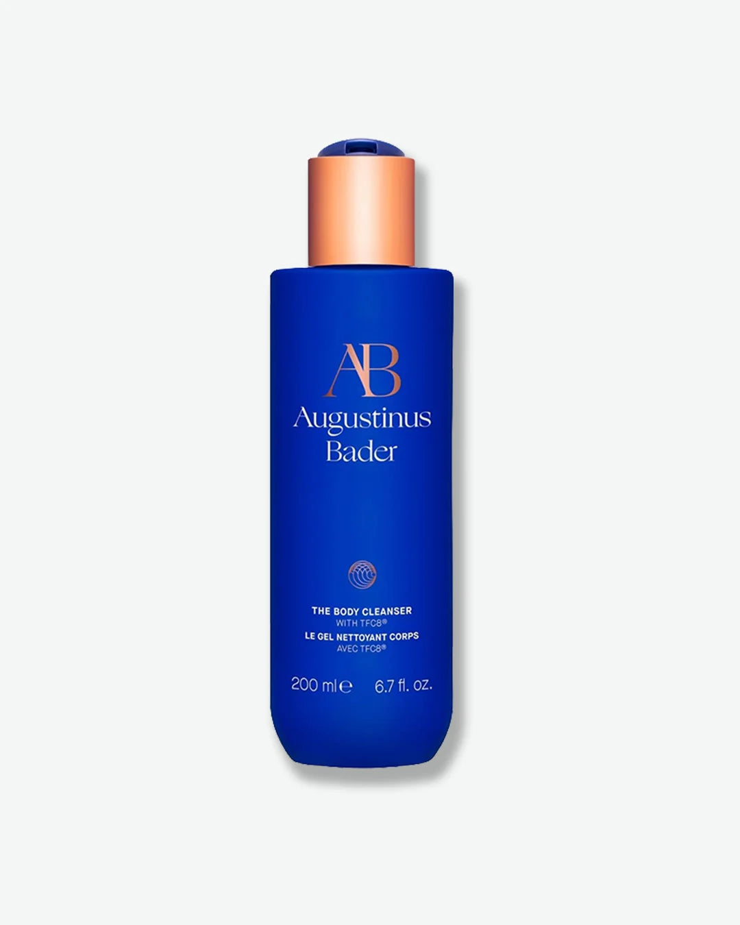 Blue Augustinus Bader The Body Cleanser bottle with a copper cap, standing a light grey background.			