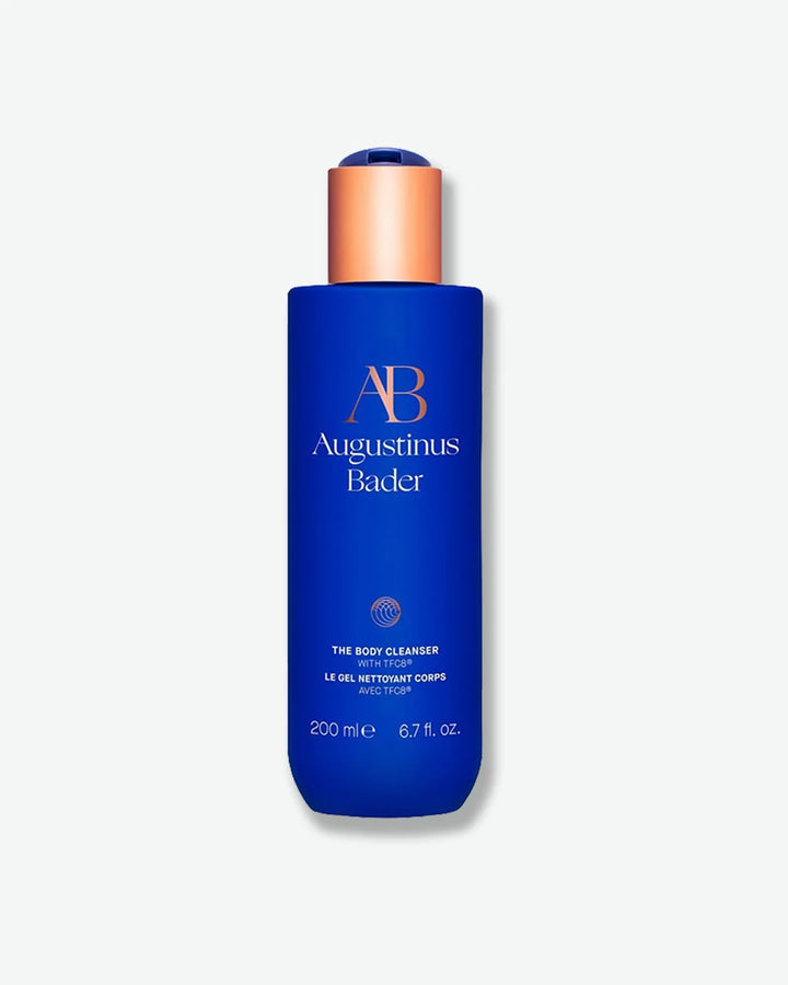 Blue Augustinus Bader The Body Cleanser bottle with a copper cap, standing a light grey background.			