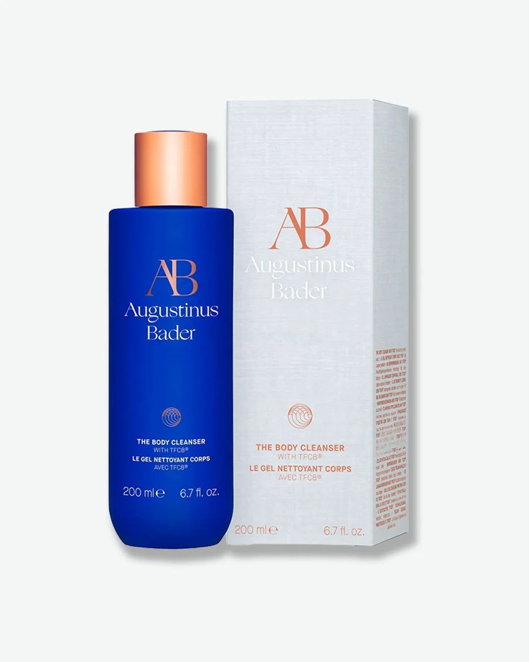 Blue Augustinus Bader The Body Cleanser bottle with a copper cap, standing next to its light gray product packaging box on a lighter gray background.