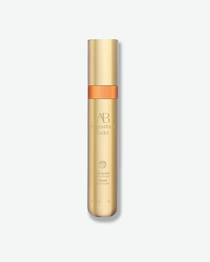Skinny gold Augustinus Bader The Elixer vial, centered against a light grey background.