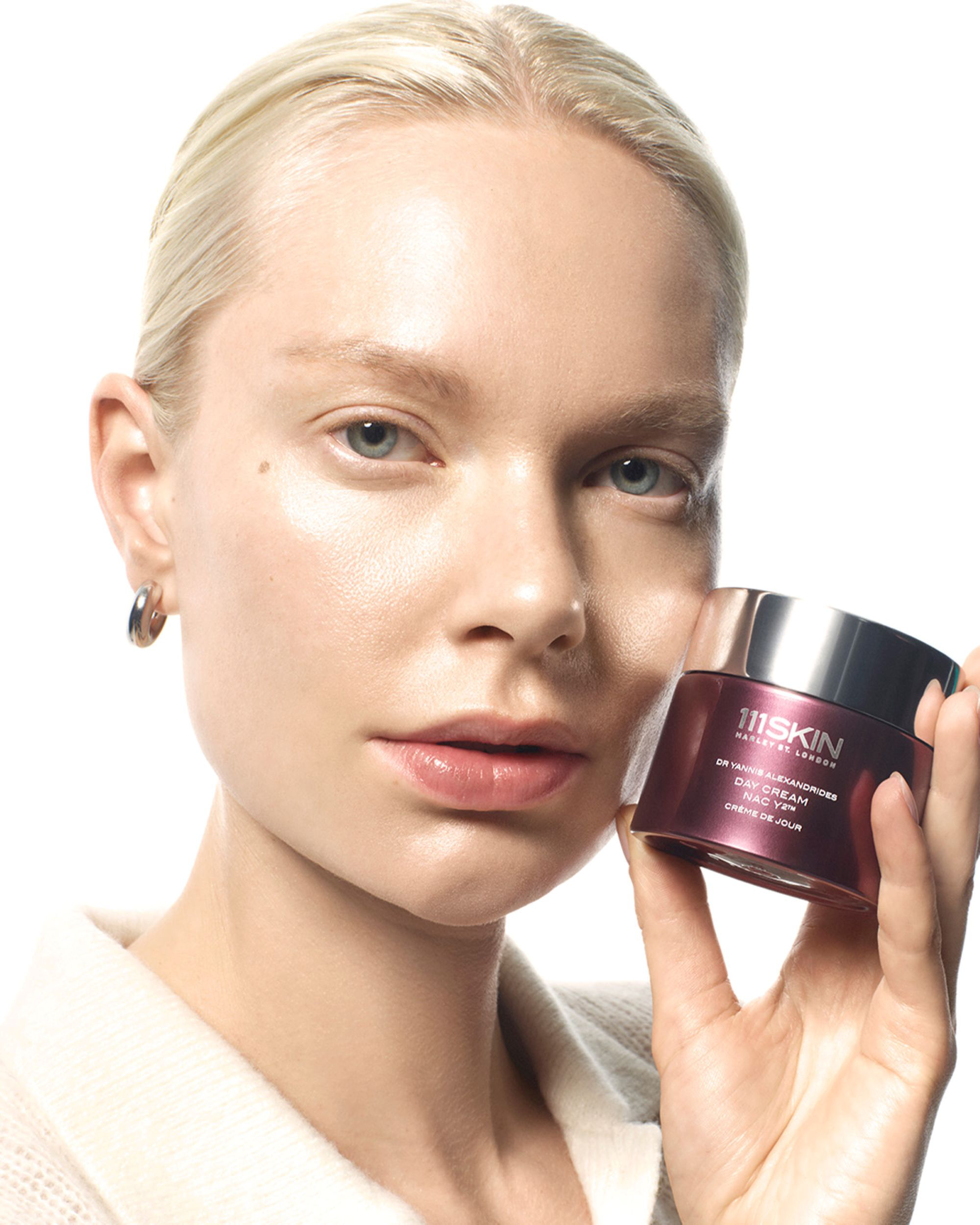 A close-up of a woman with platinum blonde hair holding a jar of TRESKIN Paris Retinol Cream against a clean white background.