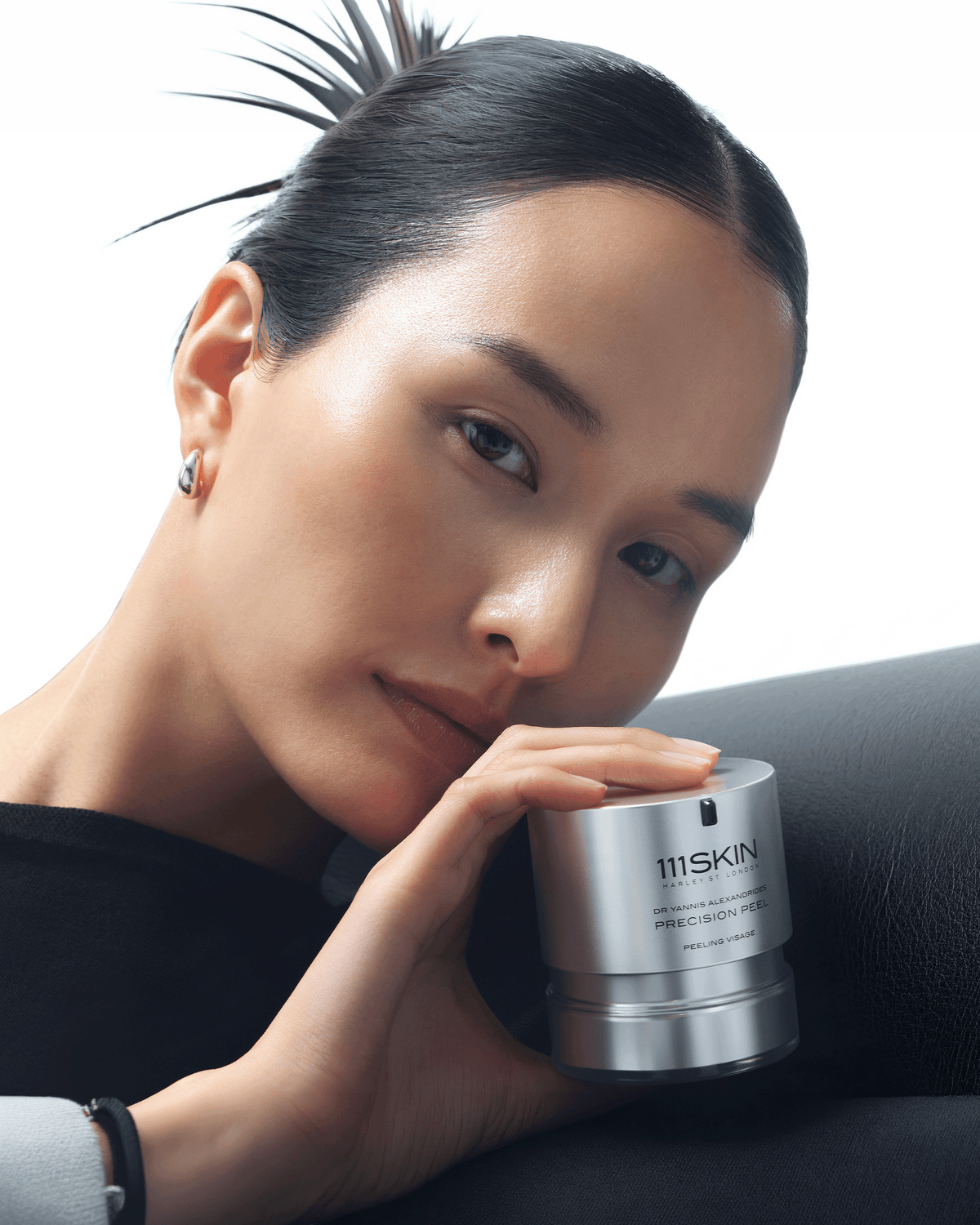 Model with slicked-back hair holding the 111SKIN Precision Peel beside her face against a minimal white backdrop.