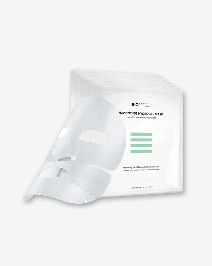 An unfolded translucent BIOEFFECT Imprinting Hydrogel Mask draped over a stacked fan of multiple white single-use mask sachets.