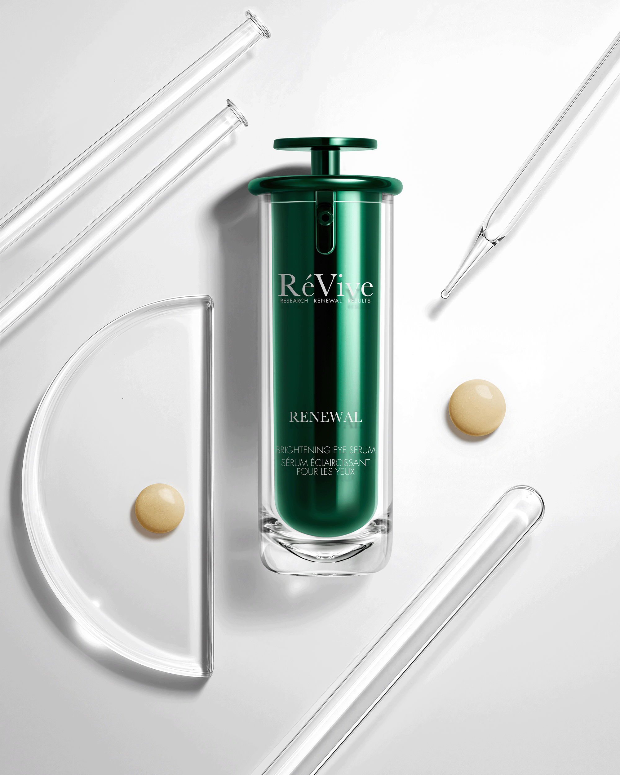 A dark green Revive Renewal skincare serum bottle is centered on a light gray background, surrounded by glass dropper pipettes, a glass half-moon, and two beige cream droplets.