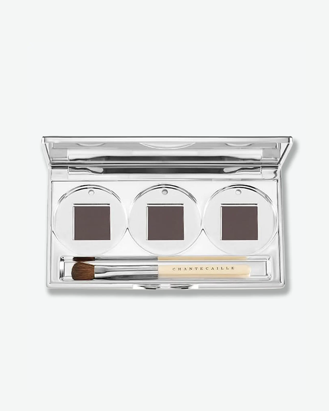 Chantecaille open silver metallic compact containing three square pans of dark brown powder, with a dual-ended makeup brush nestled inside.
