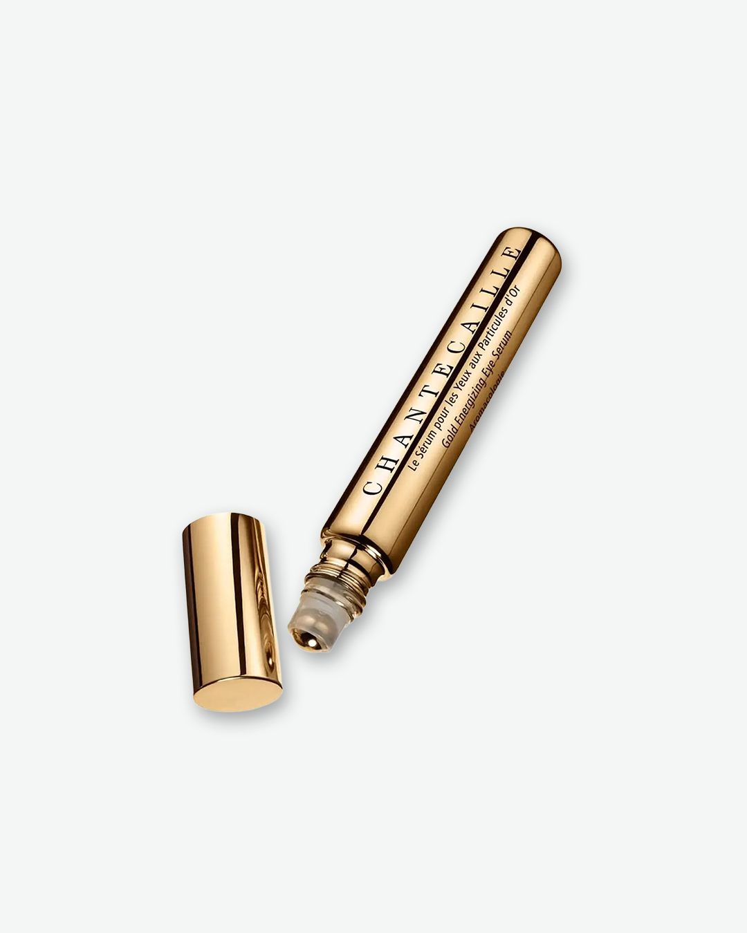 A gold rollerball eye serum tube by Chantecaille, shown lying diagonally on a plain light grey background with its matching gold cap removed and resting nearby.