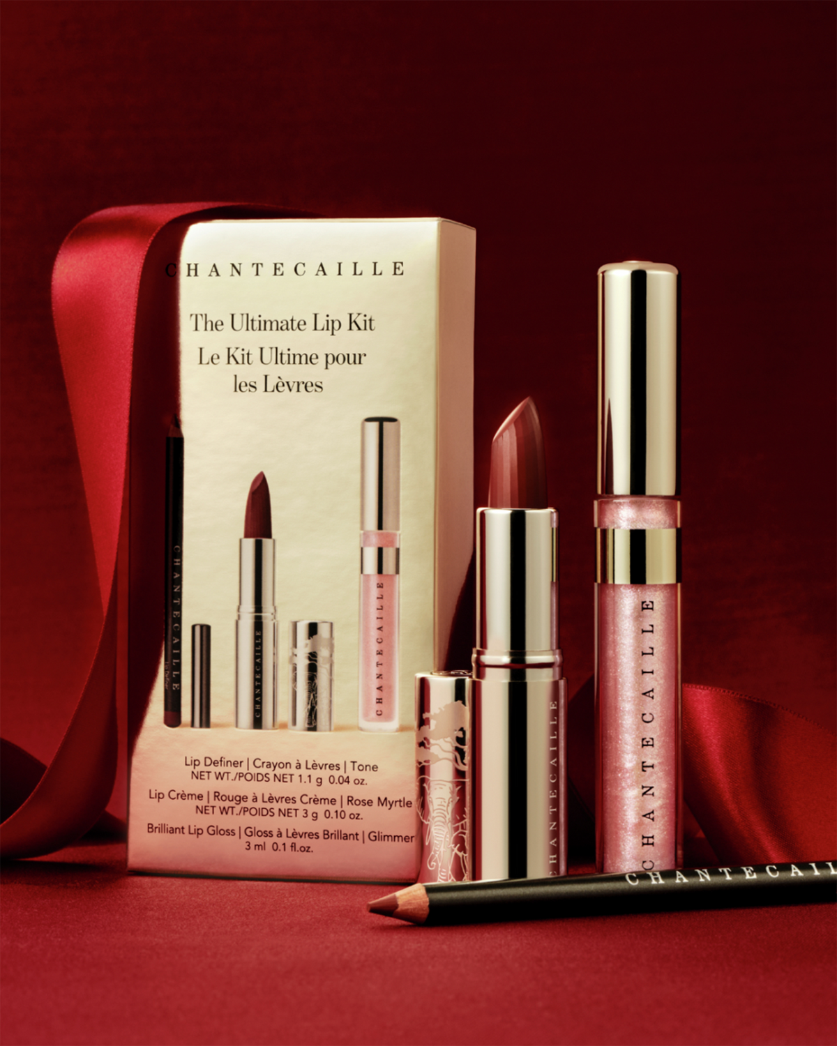 Chantecaille The Ultimate Lip Kit holiday still life featuring the lip liner, Rose Myrtle lipstick, Glimmer lip gloss, and gift packaging styled against rich red satin ribbon.