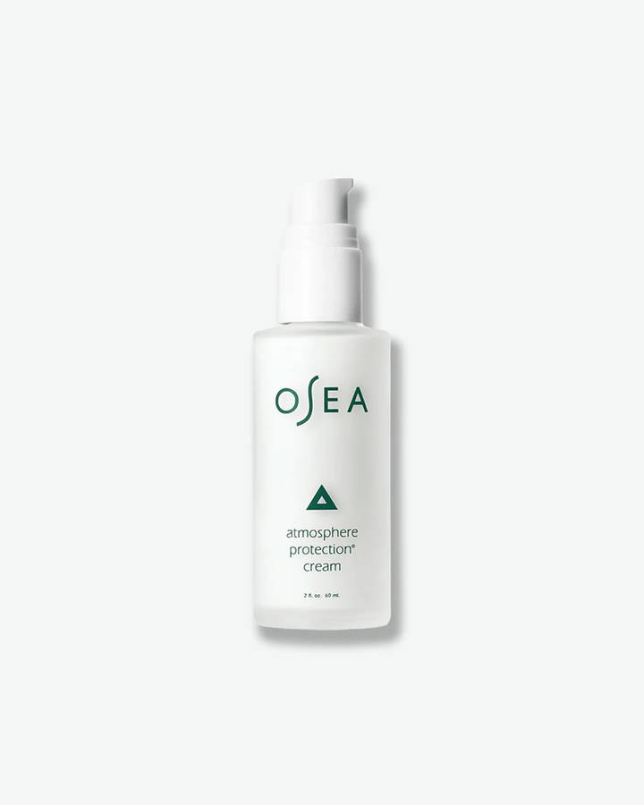 A vertical product shot of OSEA Atmosphere Protection Cream in a 2 fl. oz. (60 ml) bottle. The white cream fills a frosted glass bottle that features a matching white pump mechanism, a small dark green triangle icon, and minimalist dark green text.