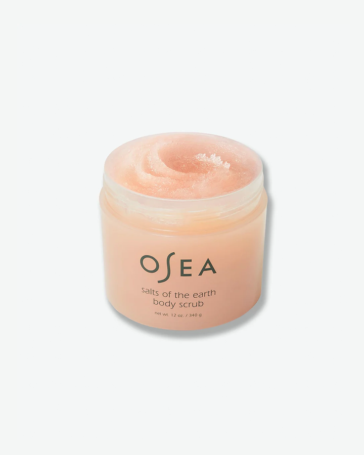 An angled, open-container shot of the OSEA Salts of the Earth Body Scrub jar with its lid removed. The thick, glistening pink-tinted salt scrub formula is visible inside the container, filling it nearly to the top.