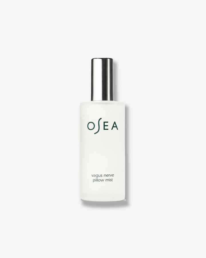A vertical product shot of OSEA Vagus Nerve Pillow Mist. The mist is contained within a cylindrical frosted glass bottle and is topped with a sleek, reflective metallic silver spray cap. The dark green OSEA brand logo and the product name are printed cleanly on the front against a plain white background.