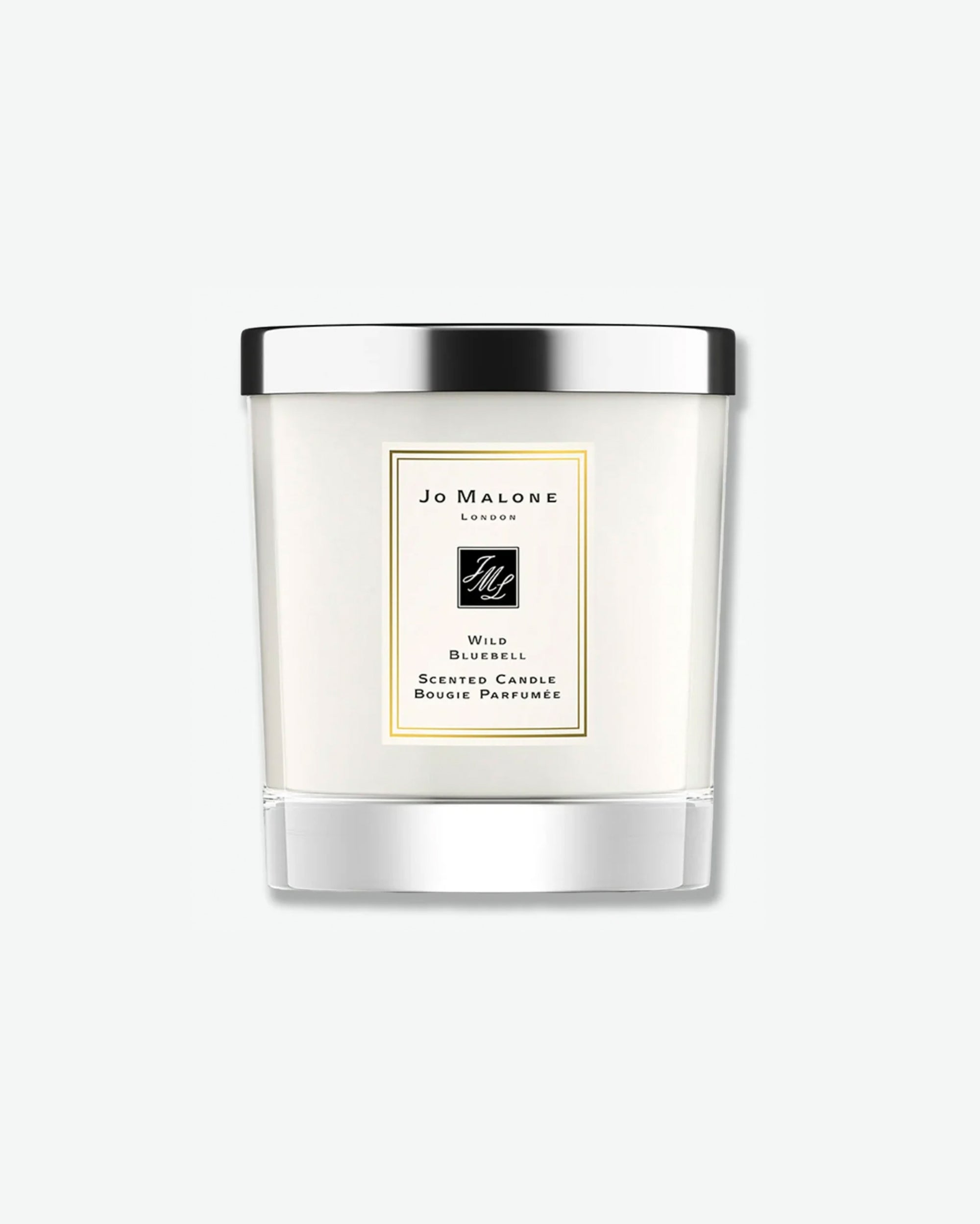 Product shot of a Jo Malone London Wild Bluebell scented candle. The white wax is housed in a clear cylindrical glass tumbler with a square, cream-colored label trimmed in gold. The candle is capped with a sleek, reflective silver metal lid and casts a soft shadow against a clean, minimalist light grey background.