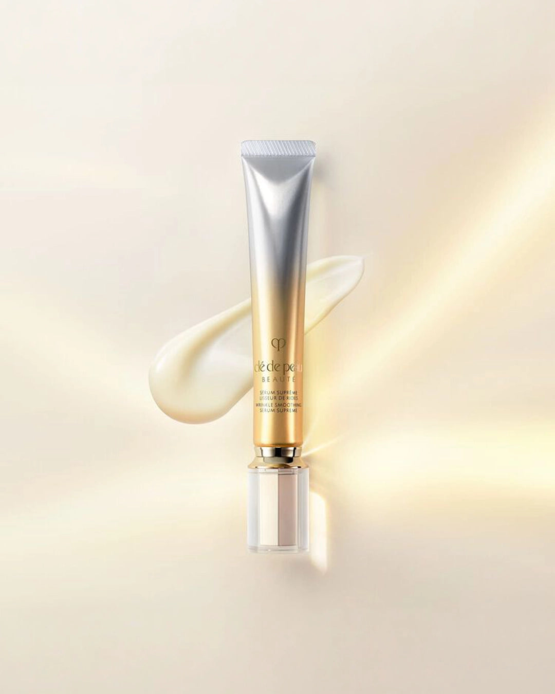 Thin silver to gold ombre colored tube with gold cap and a texture swatch behind it against a light cream colored background