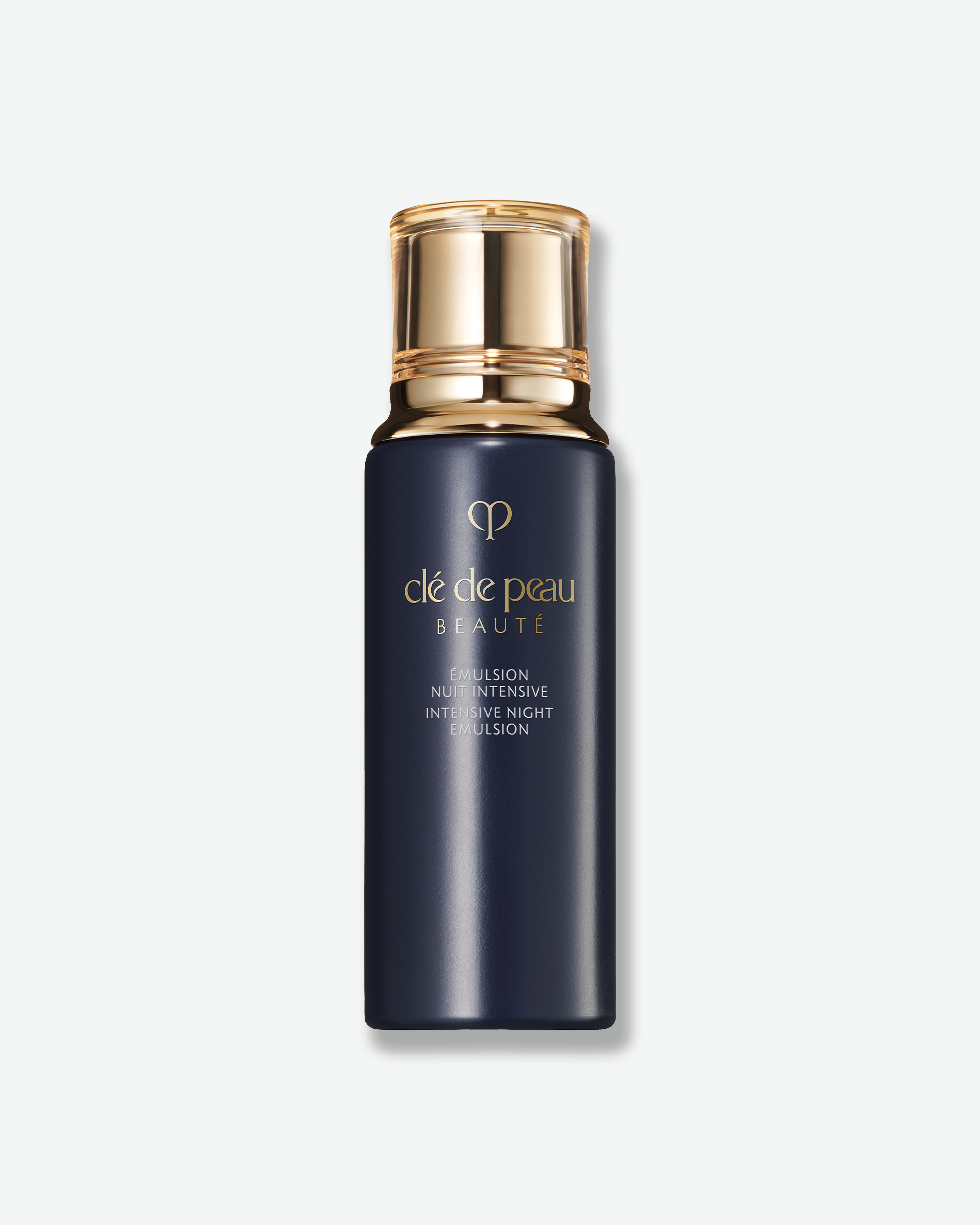A bottle of Clé de Peau Beauté Intensive Night Emulsion in a dark navy blue bottle with a shiny gold cap, centered on a light gray background.