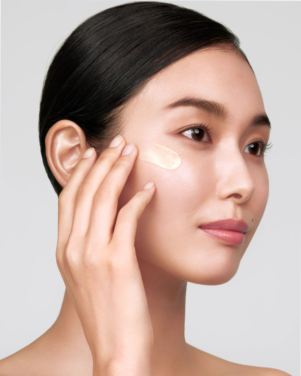 Model applying Clé de Peau Beauté Supreme Wrinkle Smoothing Serum to her cheek.
