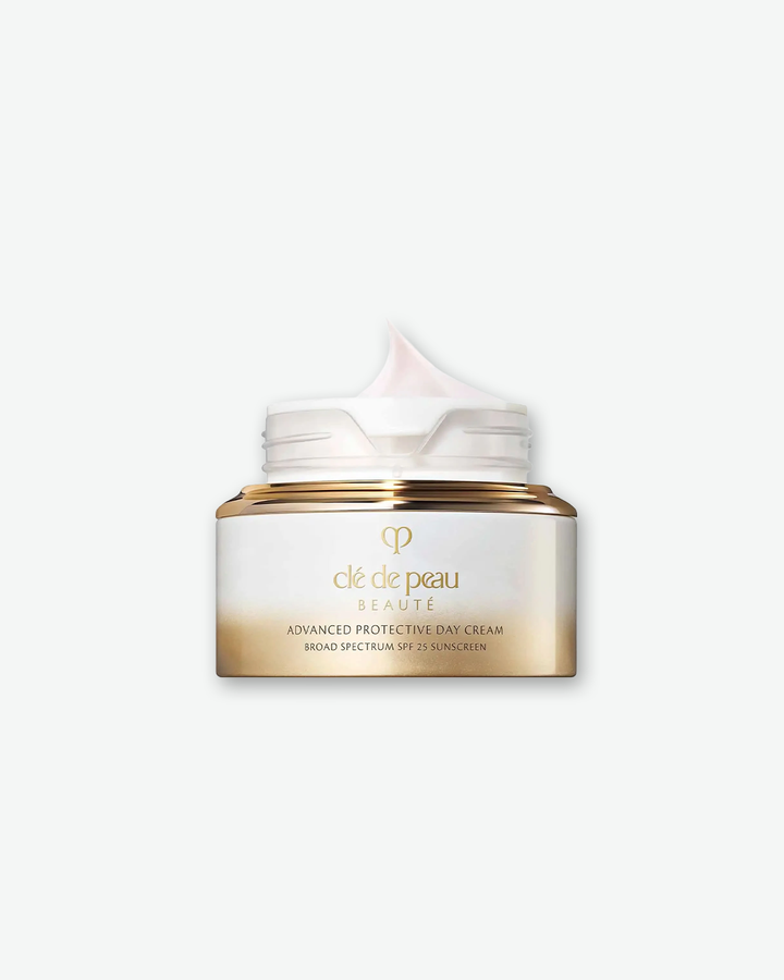 An open jar of Clé de Peau Beauté Advanced Protective Day Cream Broad Spectrum SPF 25 Sunscreen showcasing a dollop of pale pink cream inside, in an elegant white and gold ombré container against a light grey background.