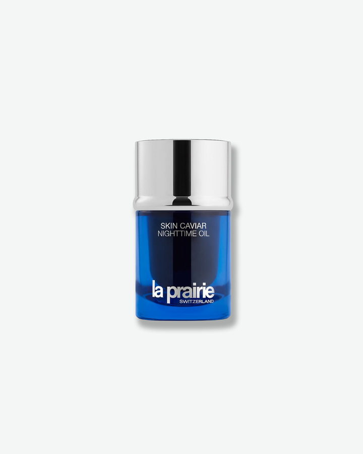 Front view of a La Prairie Skin Caviar Nighttime Oil bottle against a plain gray background. The sleek, cylindrical bottle features the brand's signature translucent royal blue glass body with silver branding, crowned by a tall, polished silver metallic cap.