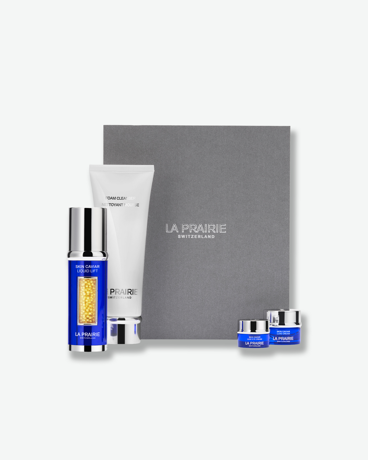 La Prairie skincare gift set featuring a gray presentation box, a white tube, a blue and gold bottle, and two small blue jars, arranged on a light gray background.