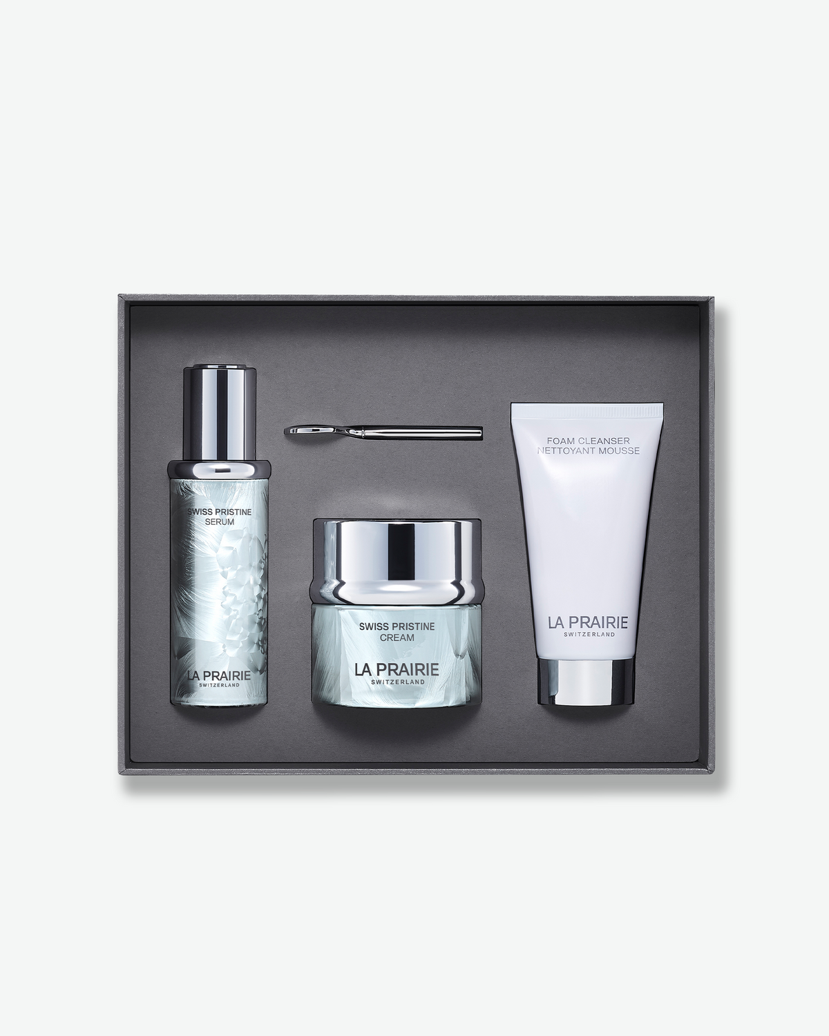 La Prairie Swiss Pristine skincare gift set featuring Swiss Pristine Serum, Swiss Pristine Cream, Foam Cleanser, and application tool arranged inside a grey presentation box.
