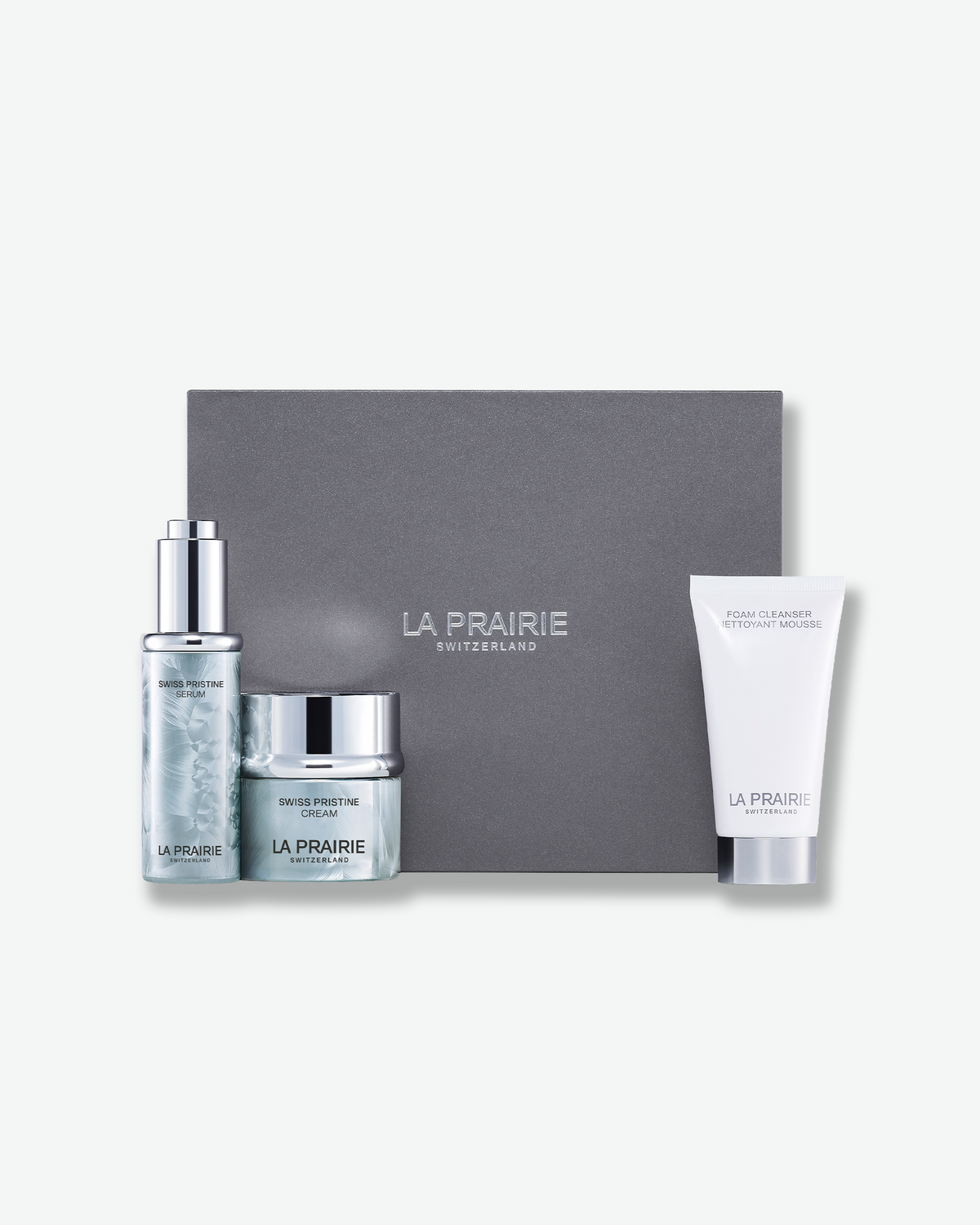 La Prairie Swiss Pristine Repairing Indulgence Set with Swiss Pristine Serum, Swiss Pristine Cream, and Foam Cleanser displayed beside a grey La Prairie gift box.
