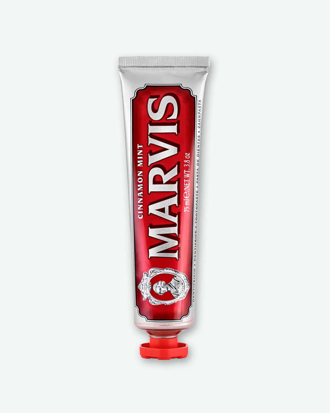 A product shot of a Marvis Cinnamon Mint Toothpaste squeeze tube, standing vertically on its cap and centered against a plain light gray background. The metallic silver tube features a glossy, deep red graphic border frame housing the large, white serif brand name "MARVIS" printed vertically. The flavor label reads "CINNAMON MINT" alongside a detailed, silver vintage portrait emblem near the bottom. The tube is capped with a matching red, sculpted decorative screw top.