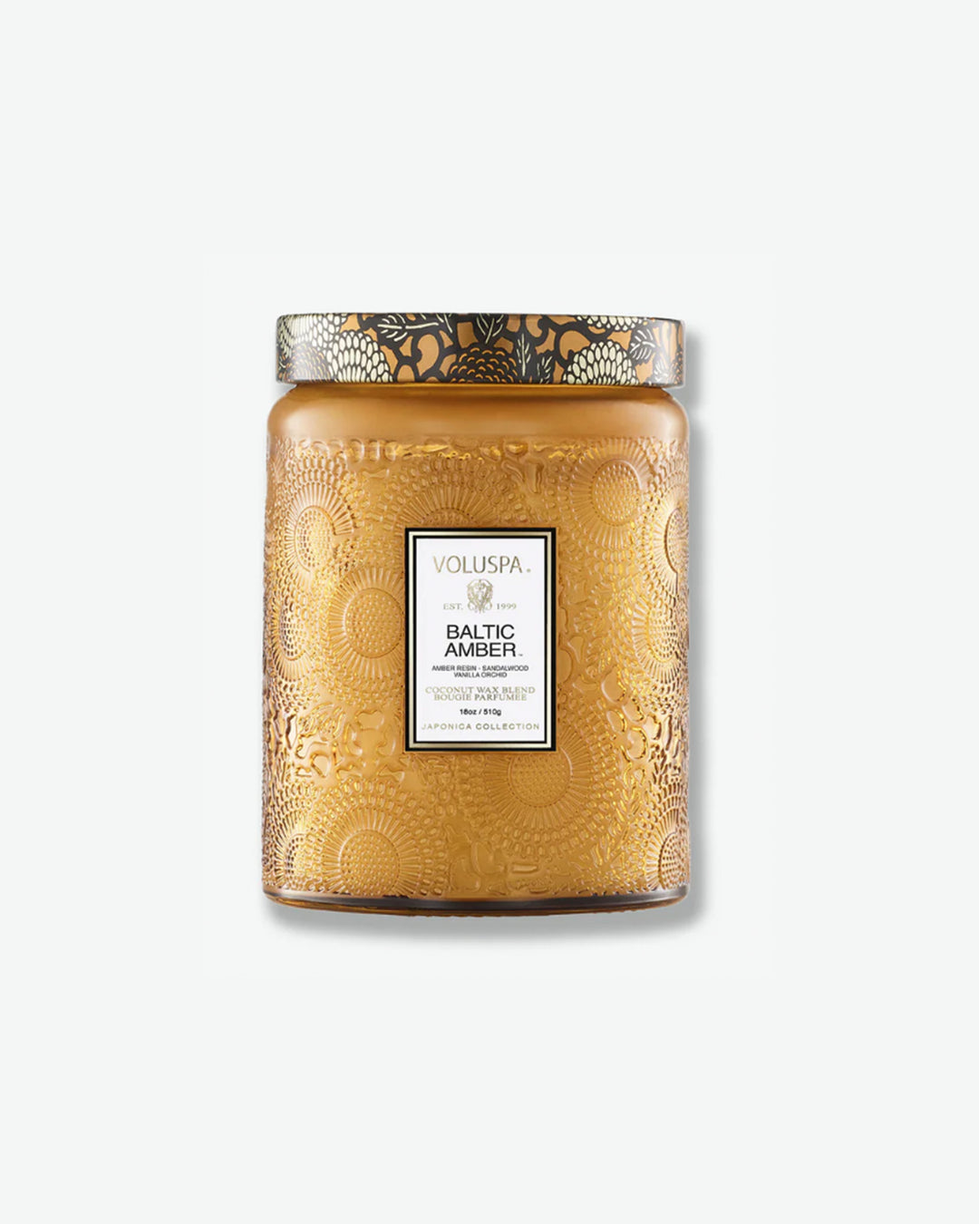 Front view of a Voluspa Baltic Amber large jar candle against a plain gray background. The candle is housed in a warm amber-colored glass jar intricately embossed with floral designs, featuring a central product label and a decorative lid matching the amber and black botanical motif.