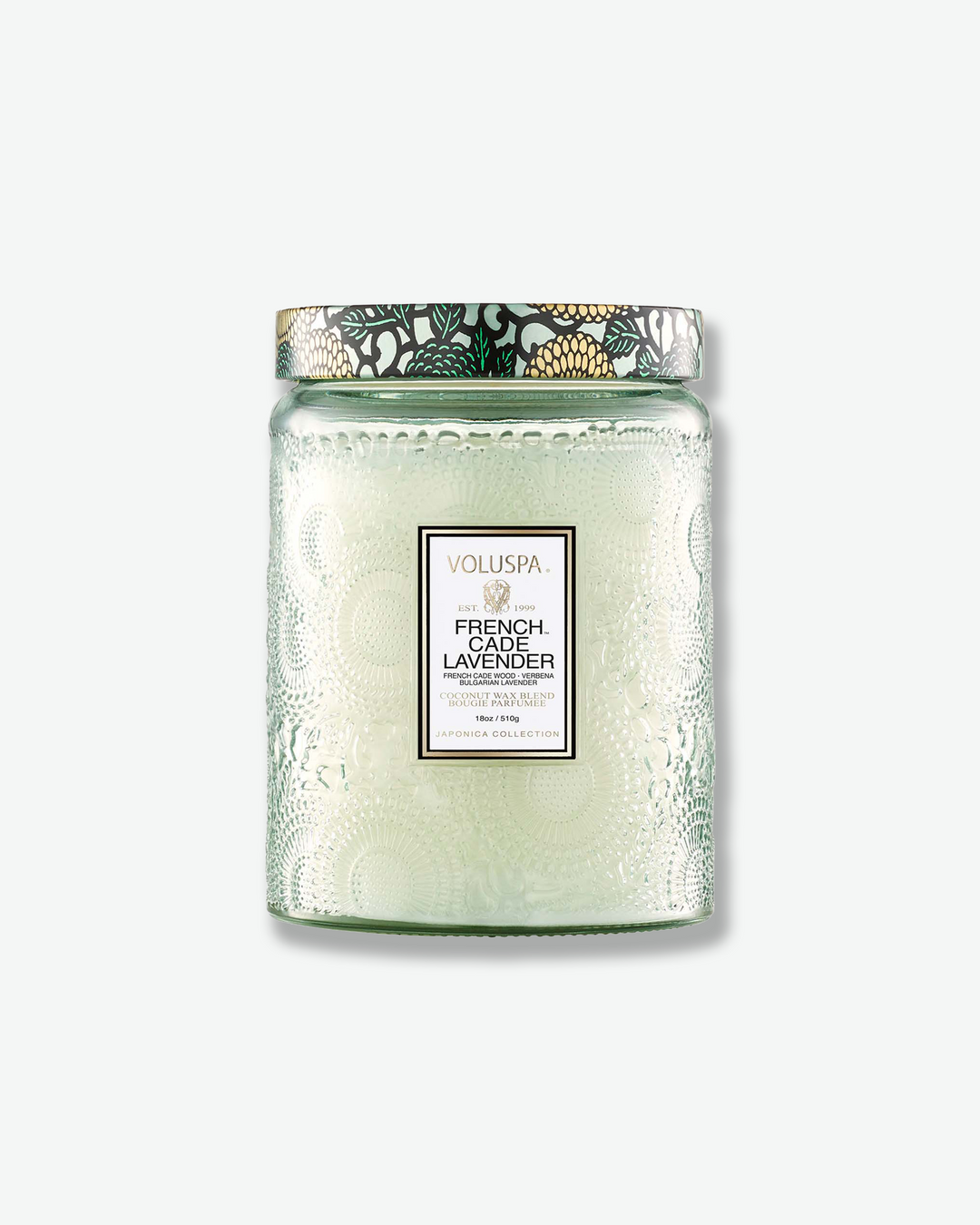 Front view of a Voluspa French Cade Lavender large jar candle against a plain gray background. The translucent, pale sage green glass jar features an intricate embossed floral texture, a central white label, and a patterned tin lid decorated with a green, black, and gold botanical design.