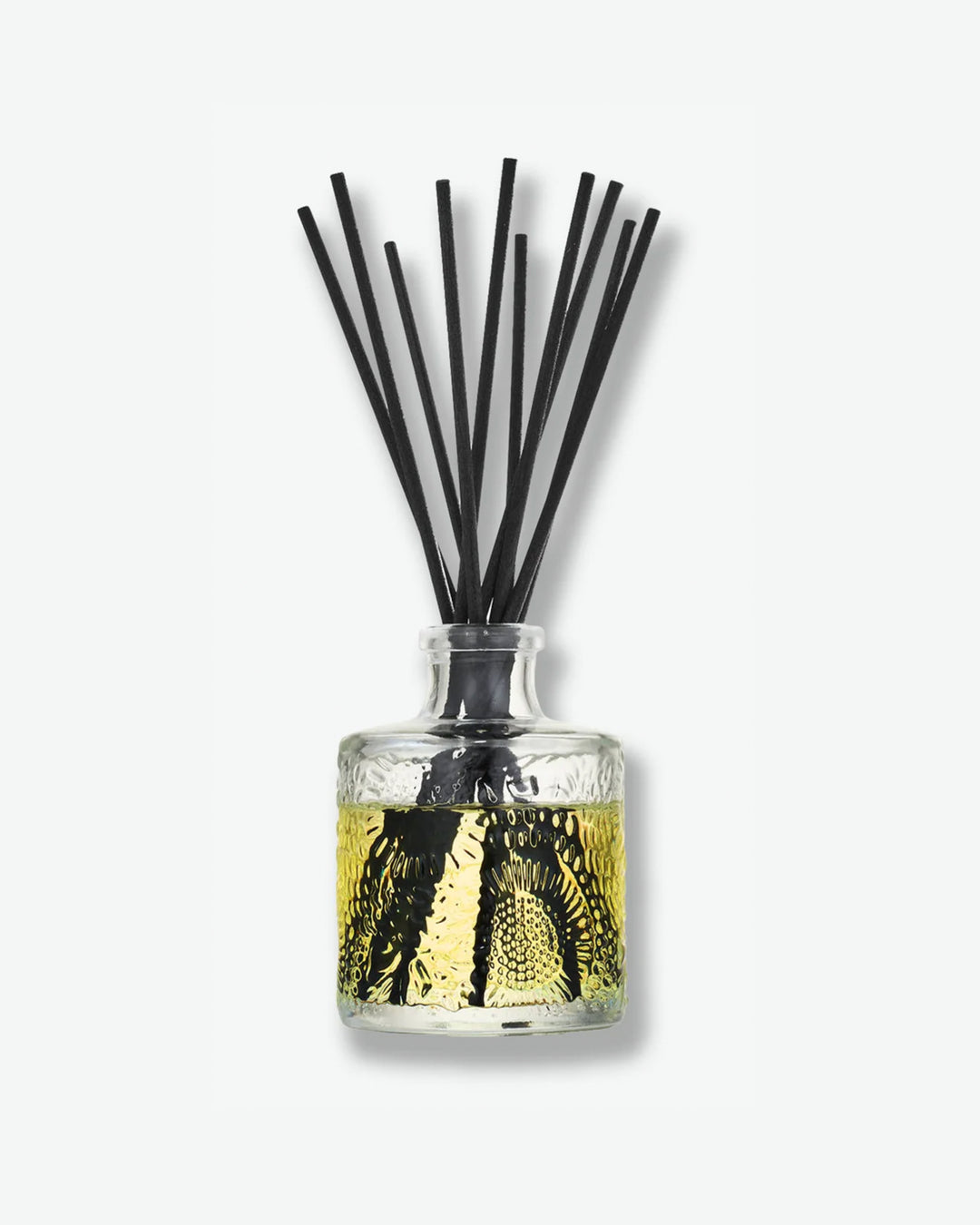 Front view of a Voluspa reed diffuser against a plain gray background. The small, clear glass bottle is embossed with a floral pattern and filled with a light yellow fragrance oil, holding a fan of thick black diffuser reeds extending vertically from the neck.
