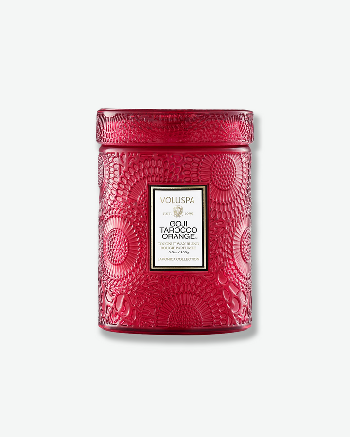 Front view of a Voluspa Baltic Amber small jar candle against a plain gray background. The warm, amber-colored glass vessel is completely detailed with an embossed floral pattern and capped with a matching textured glass screw-on lid.