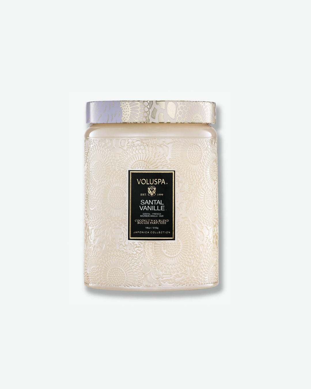 Front view of a Voluspa Santal Vanille large jar candle against a plain gray background. The candle is housed in an elegant, cream-colored translucent glass jar featuring an intricate embossed floral motif, a central product label with a gold border, and a matching patterned tin lid.