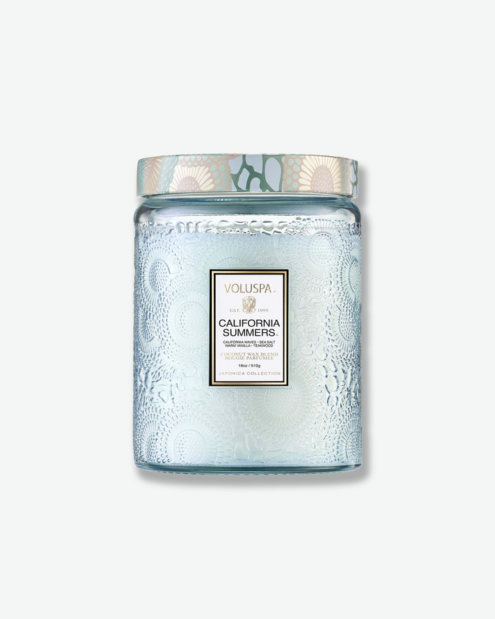 Front view of a Voluspa California Summers large jar candle against a plain gray background. The translucent, light icy-blue glass jar features a detailed embossed floral design, a central product label, and a patterned tin lid styled with a matching blue and cream botanical motif.