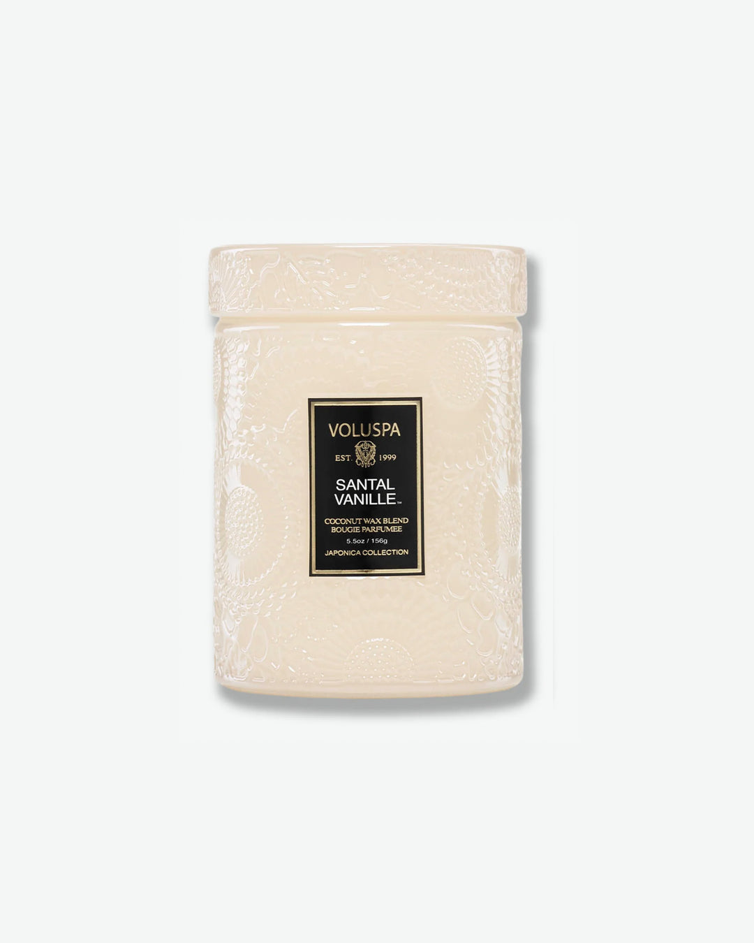 Front view of a Voluspa Santal Vanille small jar candle against a plain gray background. The candle features a cream-tinted glass body completely embossed with swirling floral designs, finished with a black and gold central label and a matching textured glass screw-on lid.