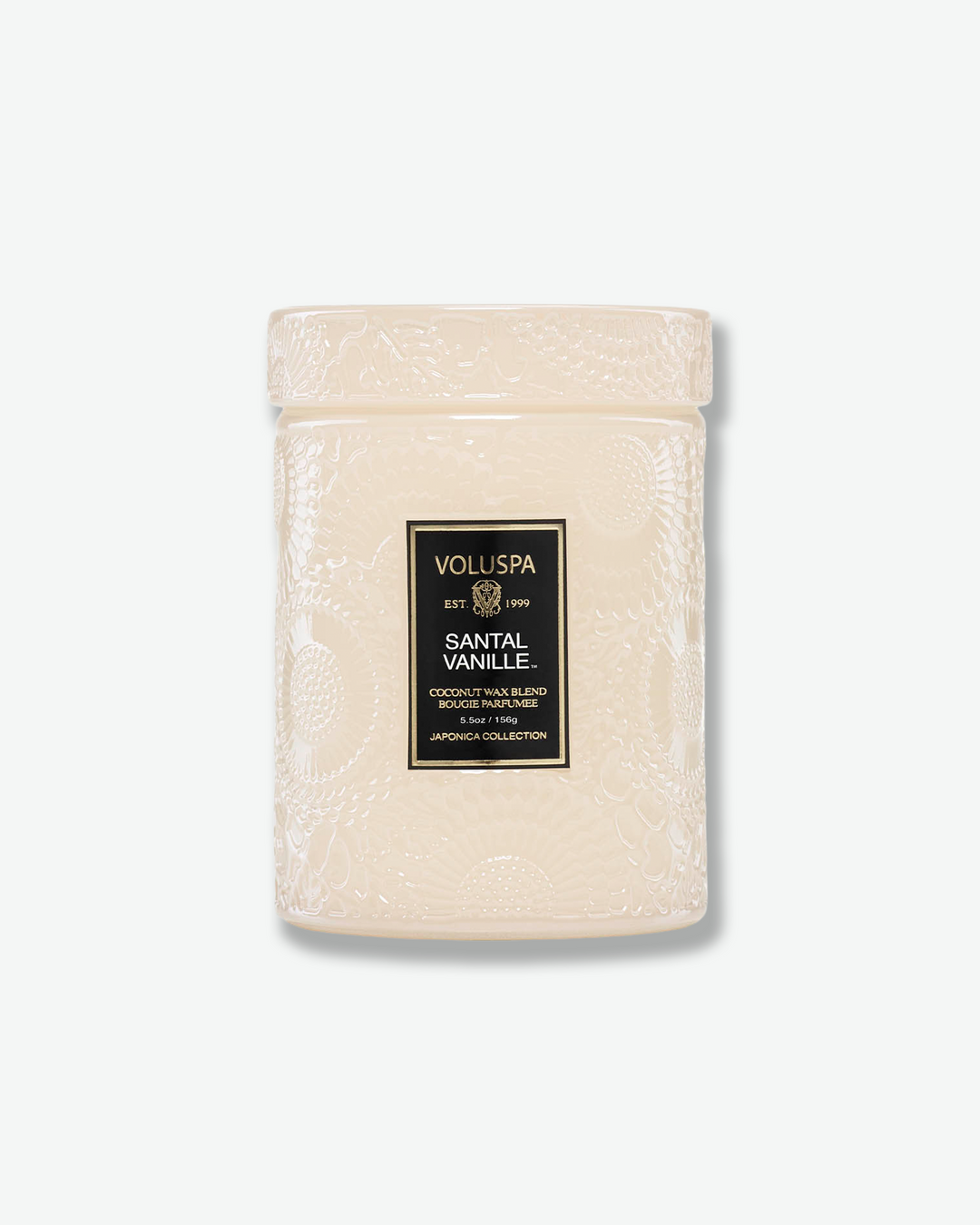 Front view of a Voluspa Santal Vanille small jar candle against a plain gray background. The candle features a cream-tinted glass body completely embossed with swirling floral designs, finished with a black and gold central label and a matching textured glass screw-on lid.